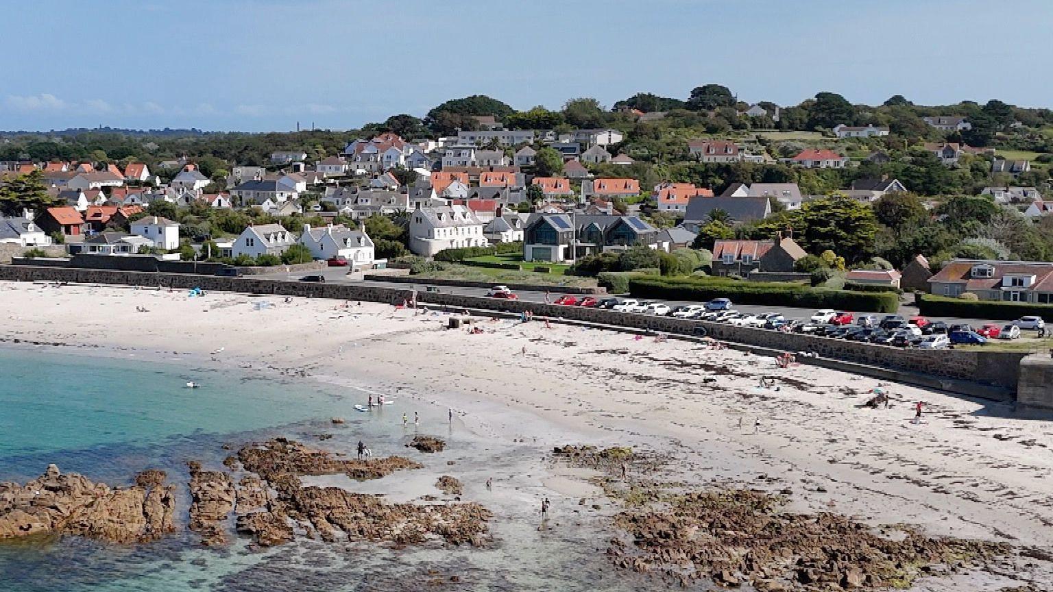 A drone view of Cobo bay showing the beach, roads housing and some of the designated parking. 