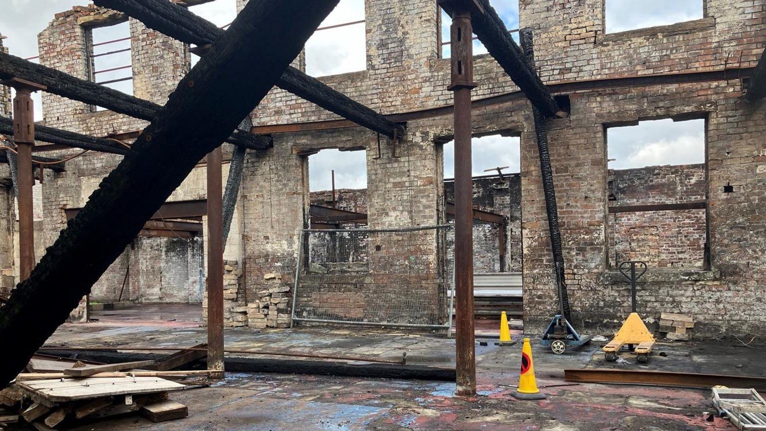 Ruined building after fire shows stone and brick walls, rusted and blackened girders and beams and empty window holes