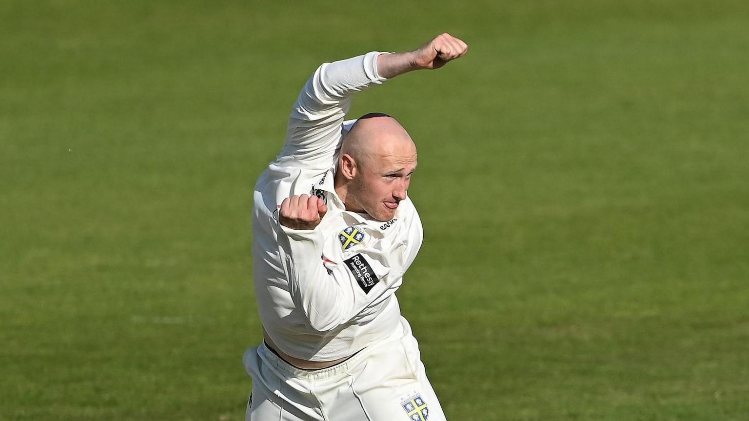 Left-arm spin bowler Callum Parkinson just after completing a delivery with his left arm tucked in and his right arm raised over his head