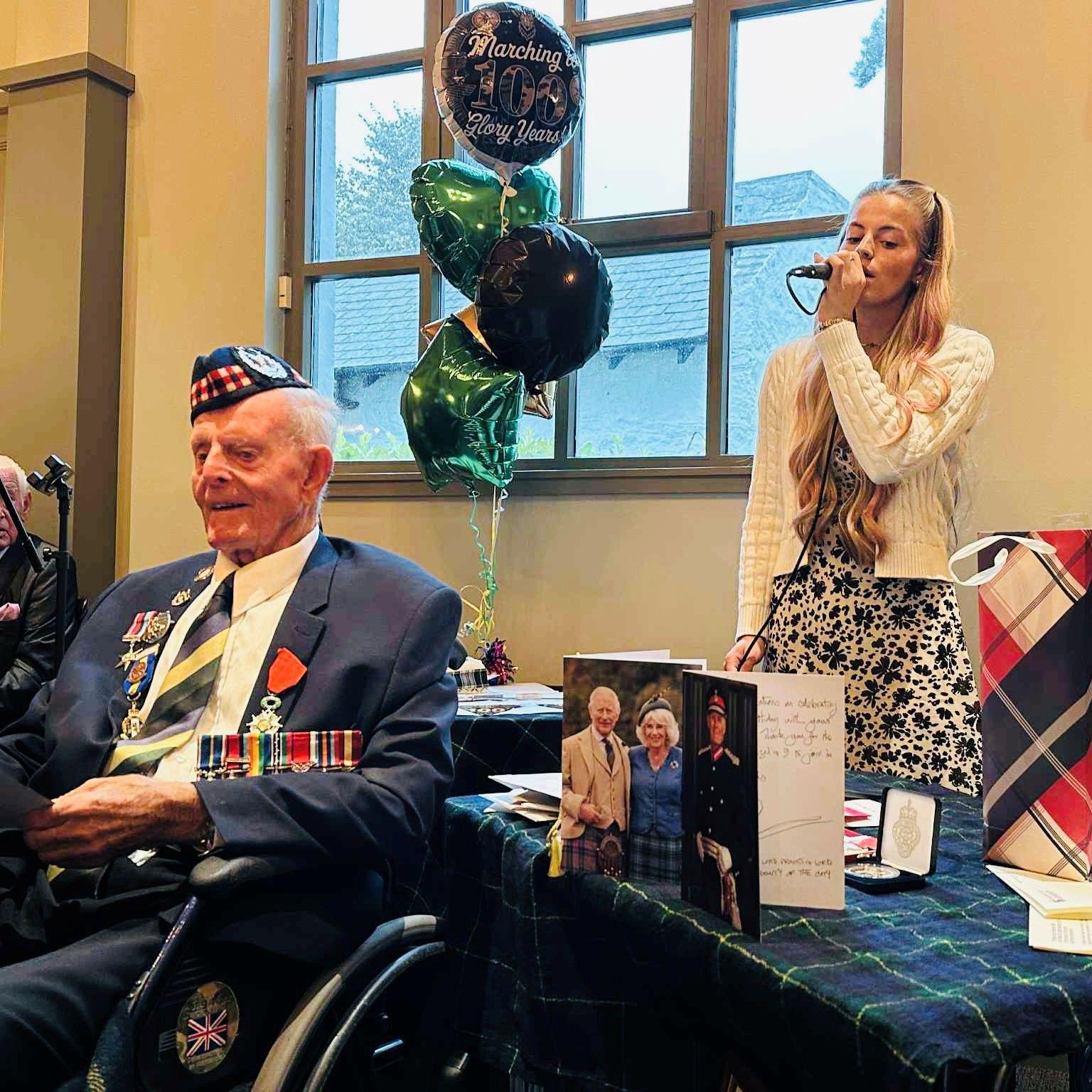Veteran Jim Glennie with 100th birthday balloons, and granddaughter singing for him.