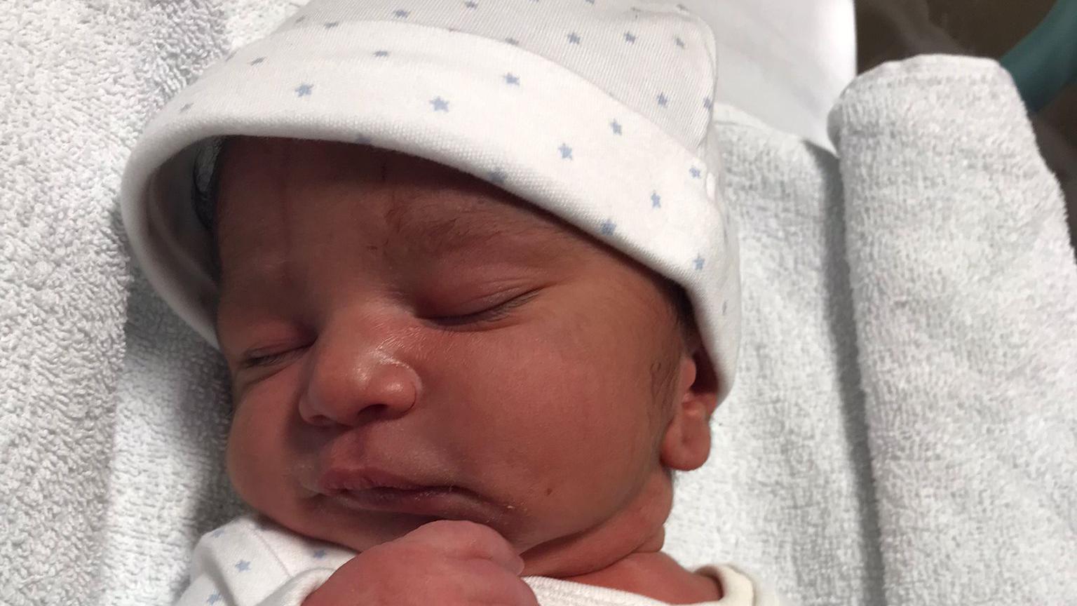 A sleeping new born baby boy wearing a white hat with grey stars. 