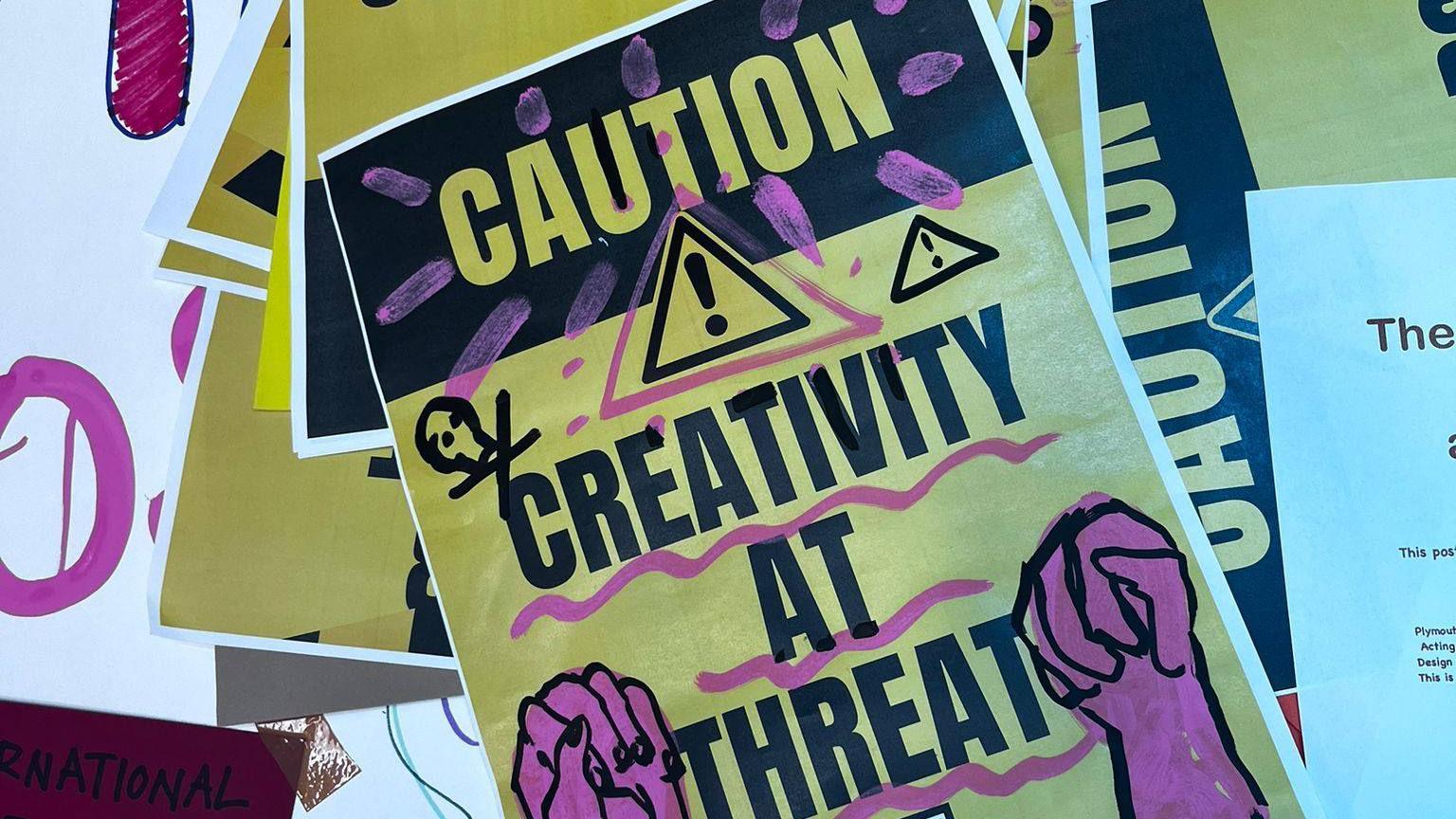 A yellow and purple poster with the words: Caution: Creativity at Threat