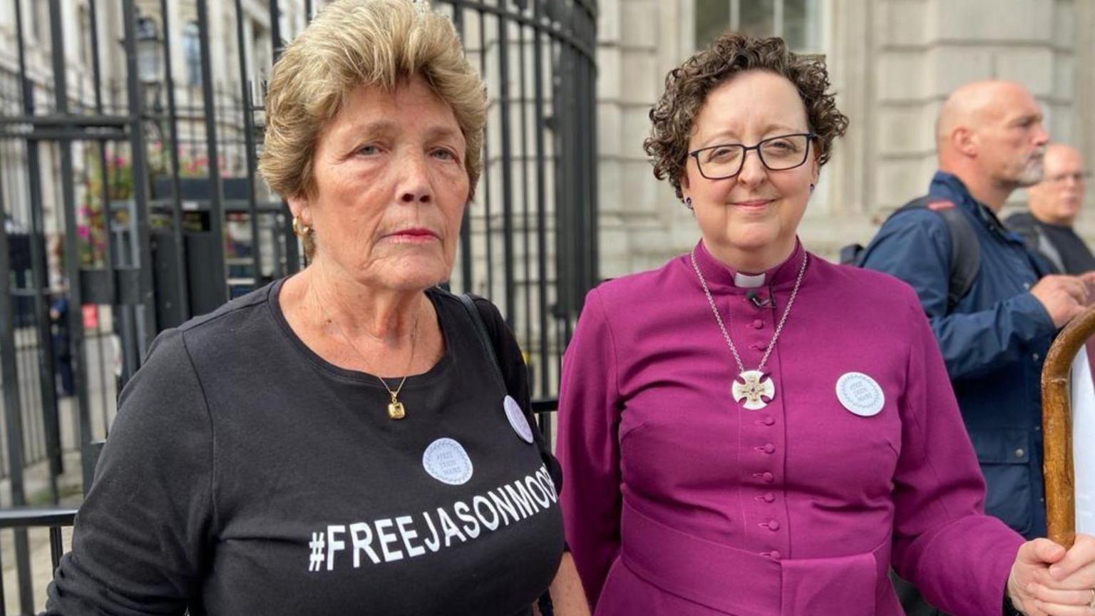 The Bishop of Stepney (right) in a purple cassock holding a crosier, next to Jason Moore's mother wearing a t-shirt reading 'free Jason Moore' 