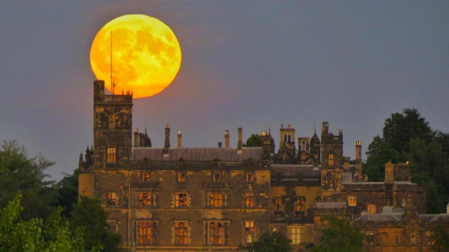 The moon lit up in yellow above a stately home in Baxterley Warwickshire 