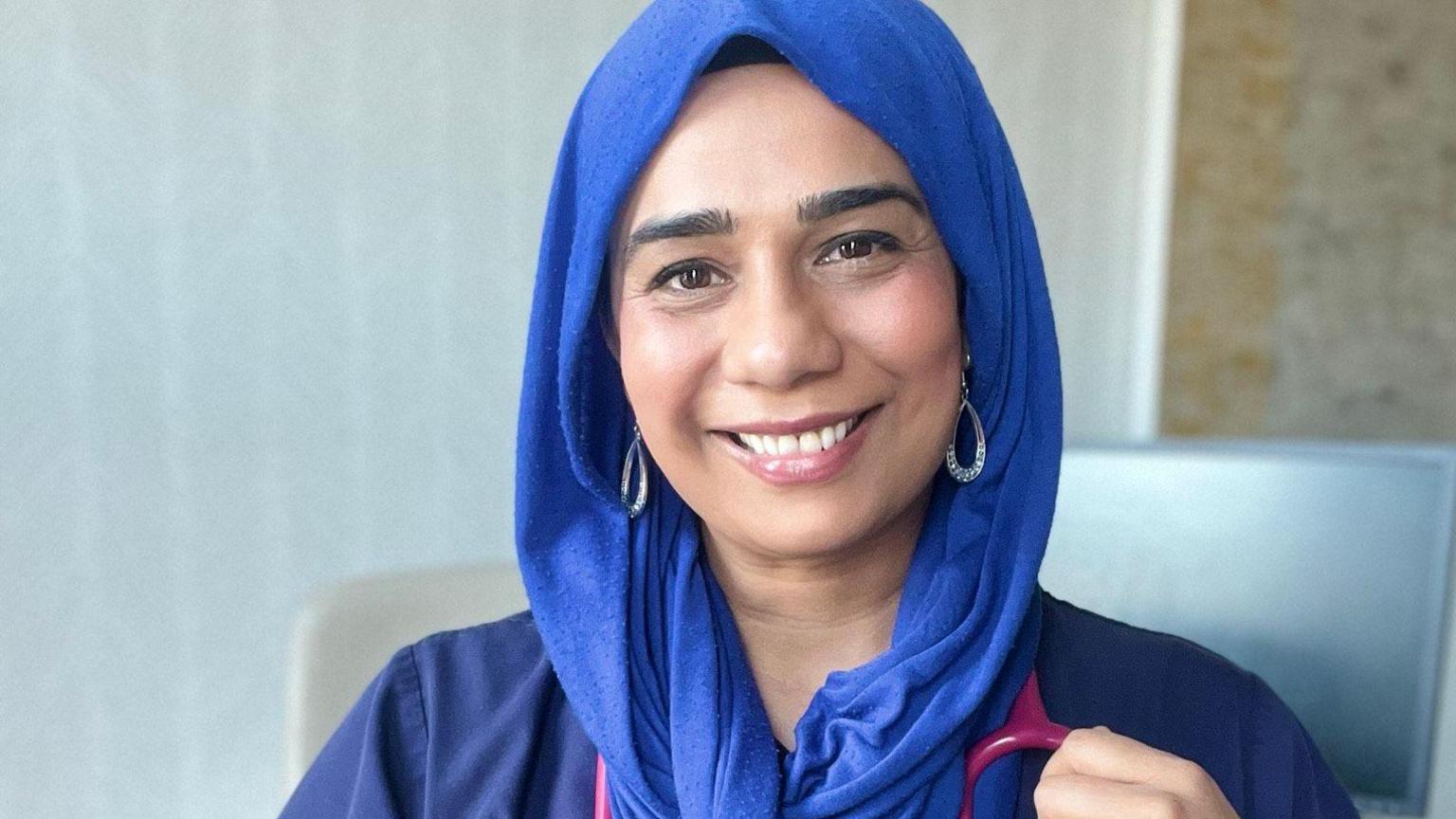 A smiling Dr Nighat Arif looking directly at the camera, dressed in a blue headscarf