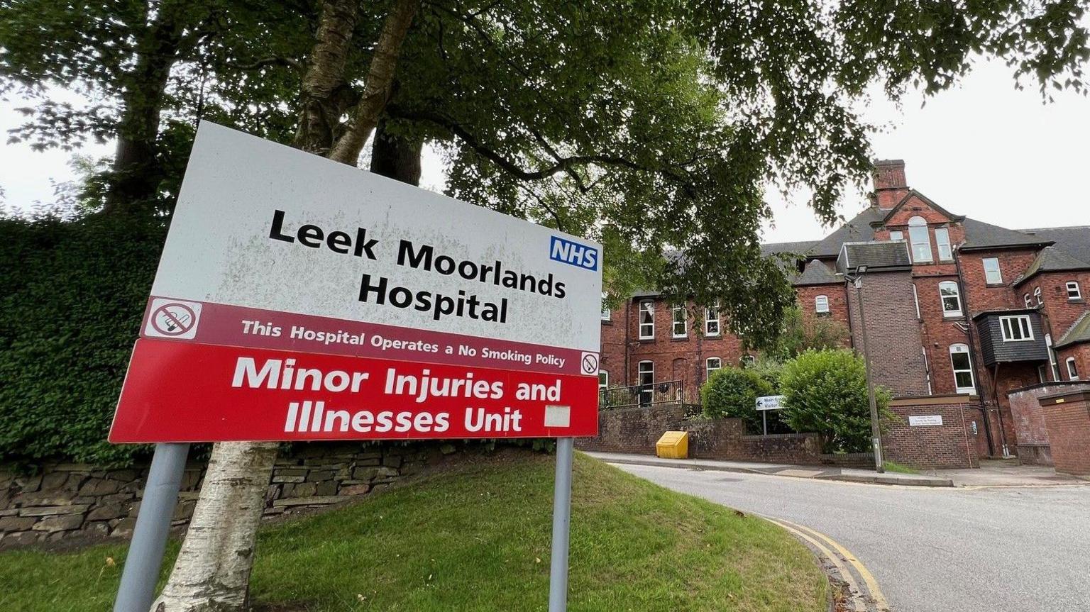 A white sign with black letters that read Leek Moorlands Hospital,  with a red sign underneath identifying it as a minor injuries and illnesses unit.