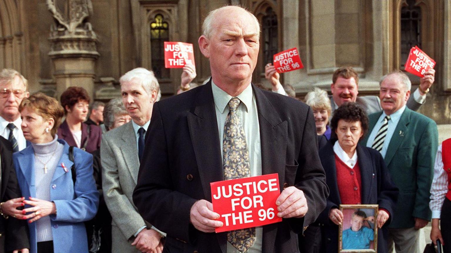 Phil Hammond holds up a small red Justice for the 96 sign as he heads up a demonstration by the Hillsborough families outside the Houses of Parliament.