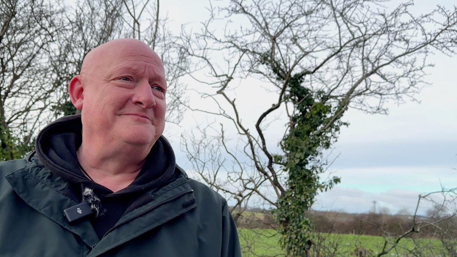 Local resident Jonny Wilde, wearing a blue coat and black fleece, stands in front of a field.