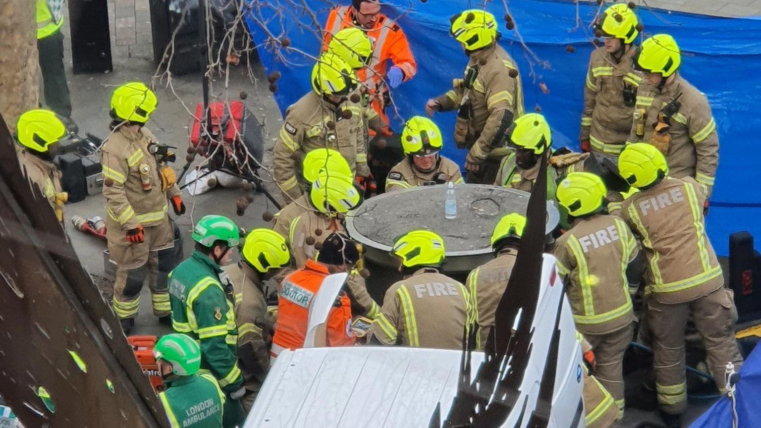 Aerial view of emergency services attempt to lift pop-up urinal in front of blue tarpaulin 