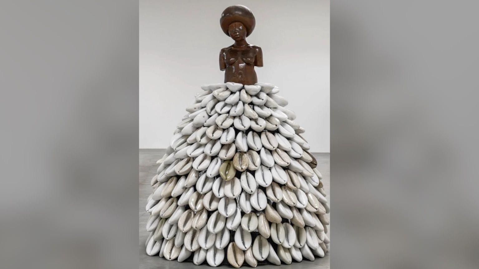 A sculpture of a black torso of a woman wearing what looks like a dress make up of dozens of large white shells