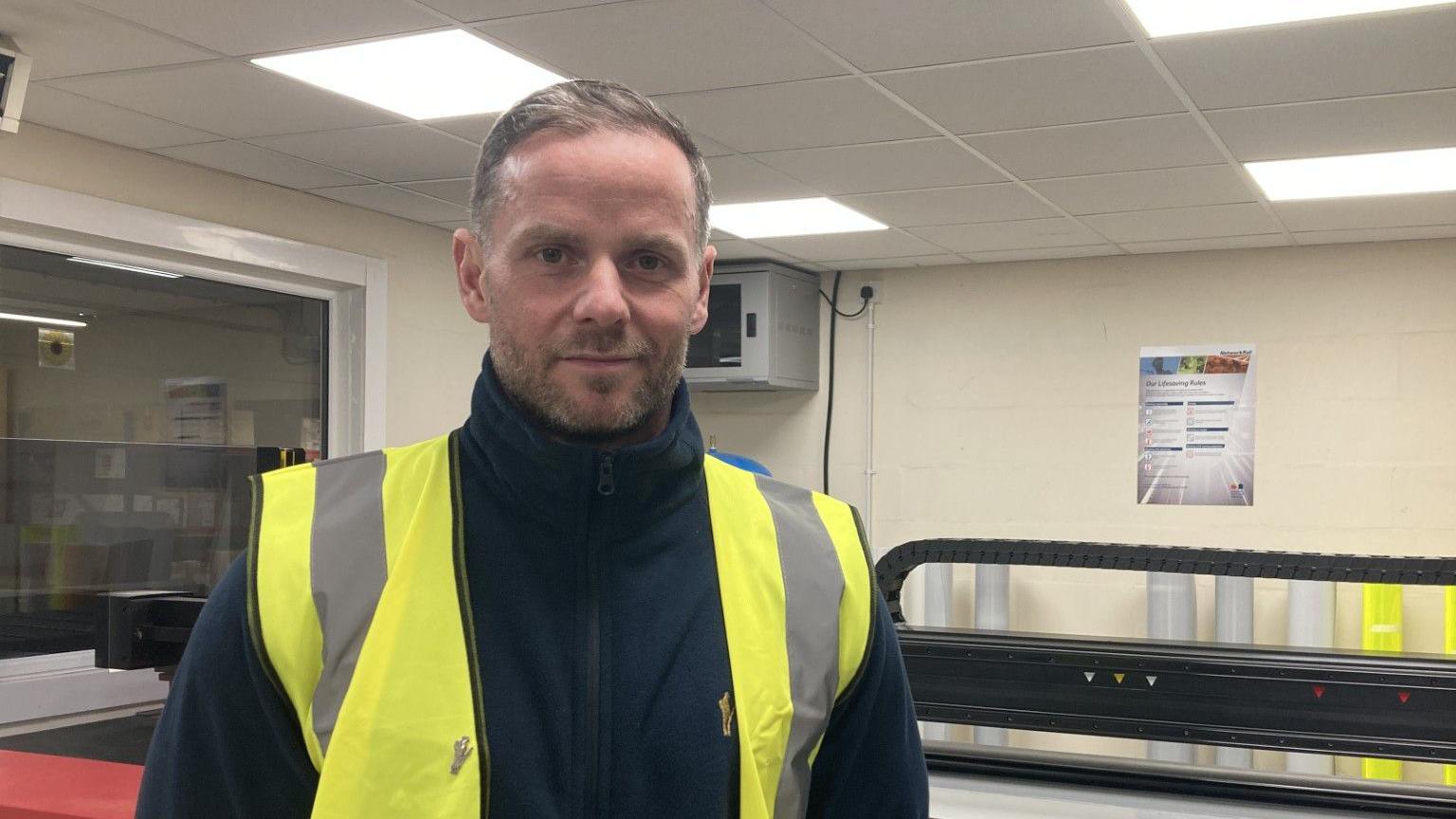 A picture of RBLI Factory Operations Manager David Church in the current facility. David is wearing a navy hoodie and a high-viz vest. 