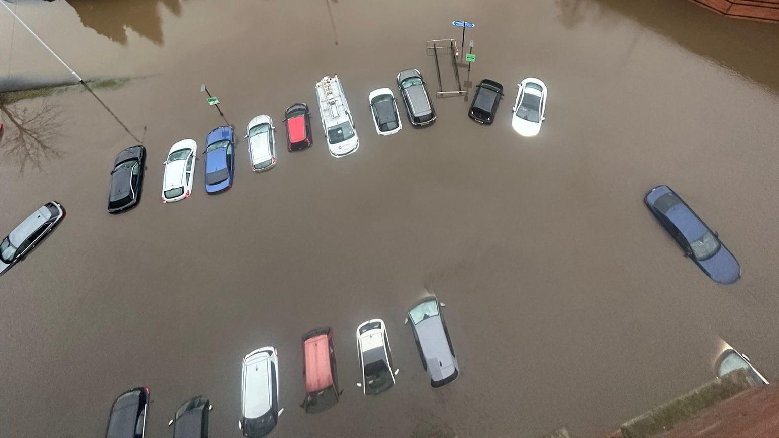 A number of cars are almost totally submerged in brown muddy flood-water