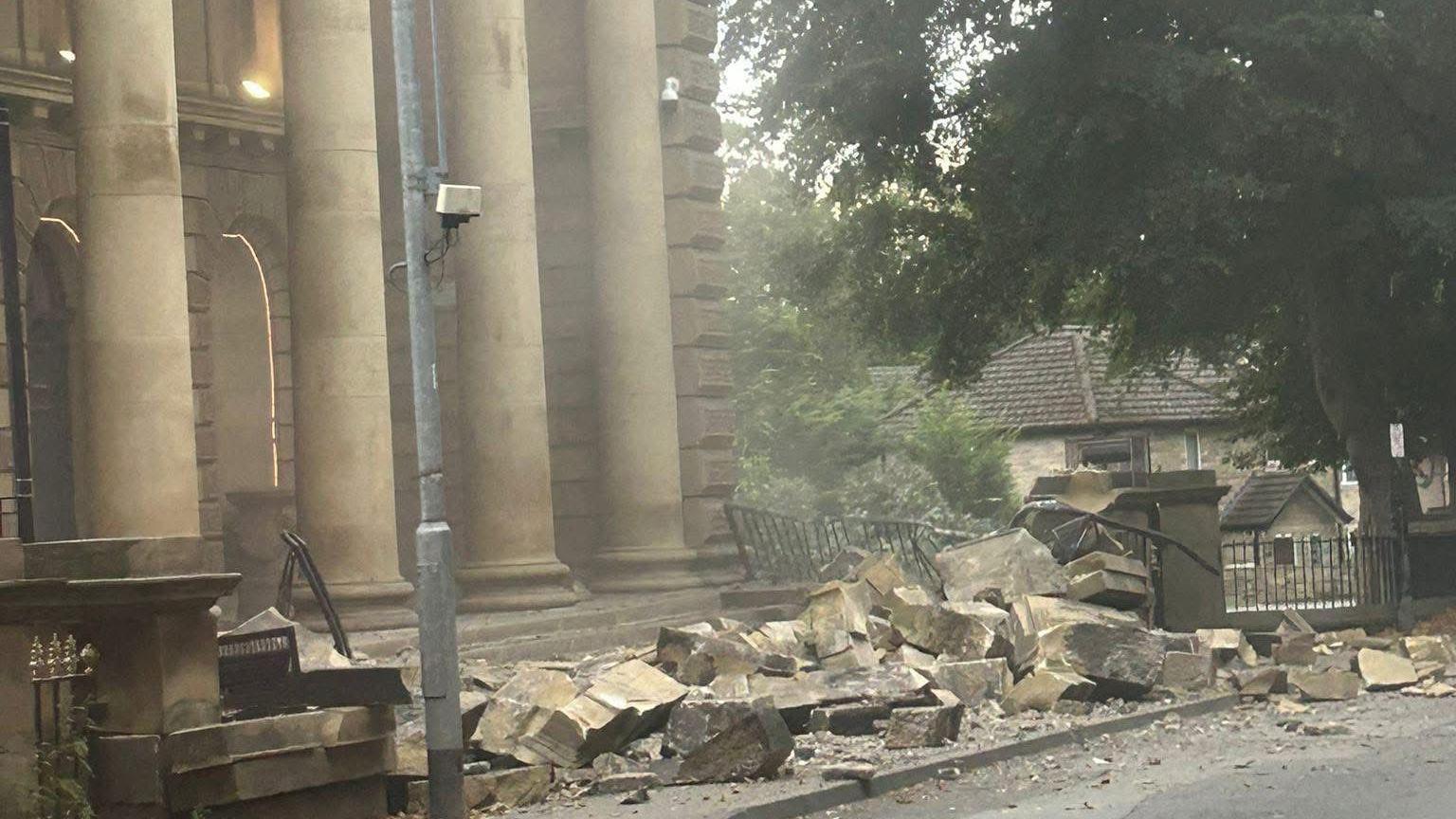 Chunks of stone masonry on a pavement outside a building with large stone columns.