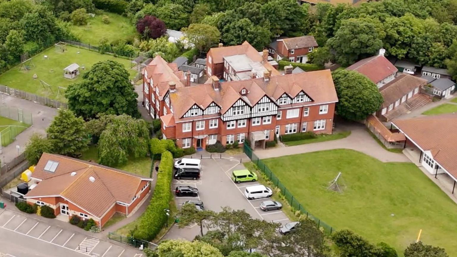 An aerial view of Bradstow School showing a large school building and its surrounding grounds. There are a number of smaller nearby buildings.