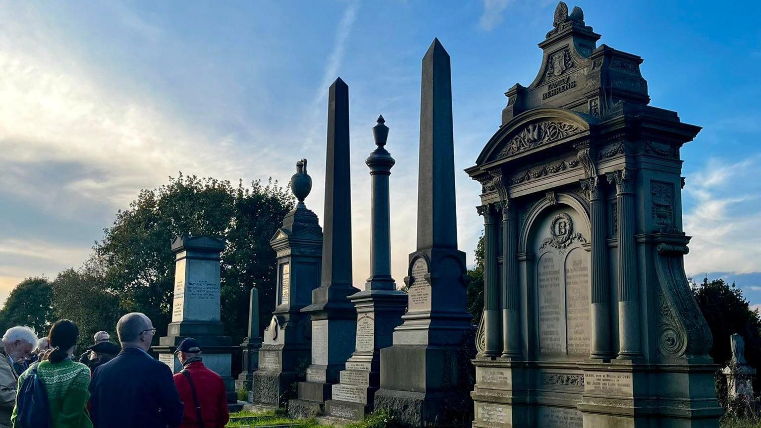 A group of people walk around a cemetery with large ornate headstones