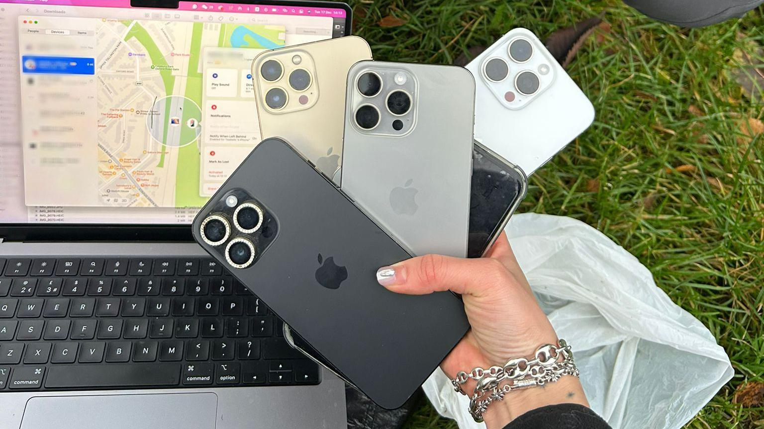 Izzy's hand holding five of the mobile phones. The carrier bag is on the ground in the background, as well as her laptop, showing the tracking map