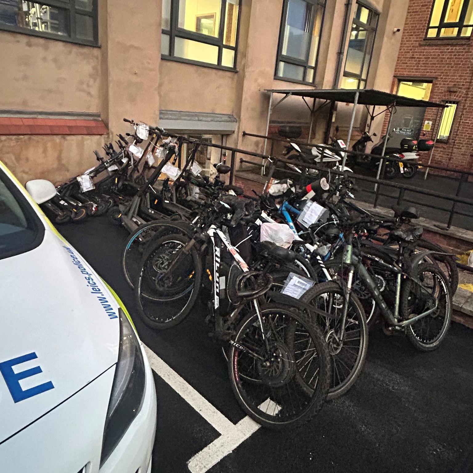 Seized e-scooters and e-bikes are pictured piled next to a police car