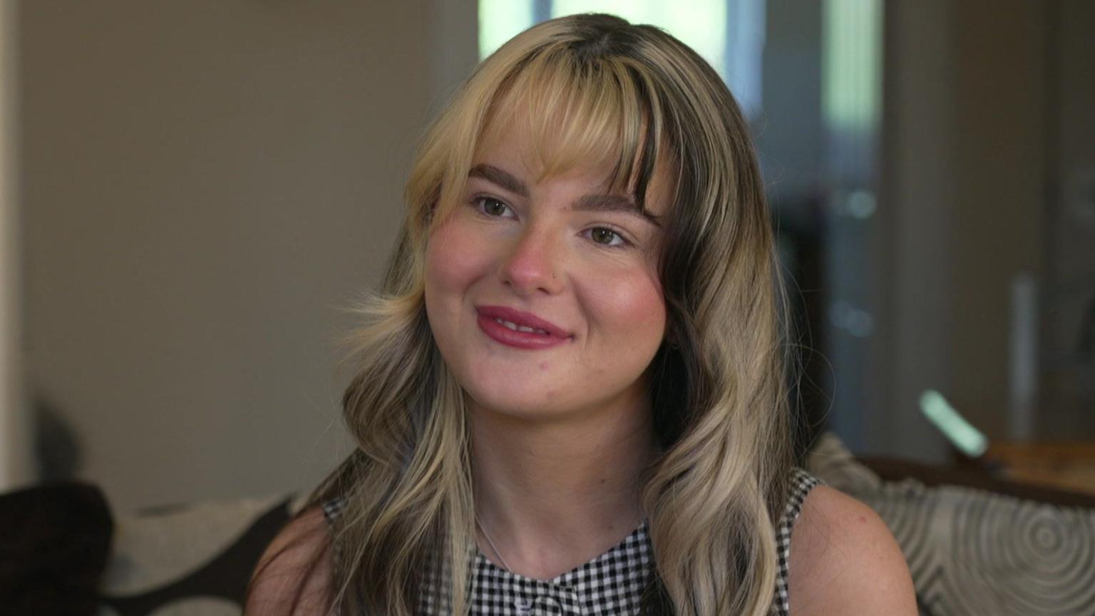 Jessica-Rae Williamson is staring off camera at the interviewer. She is smiling and is sitting in her living room. 