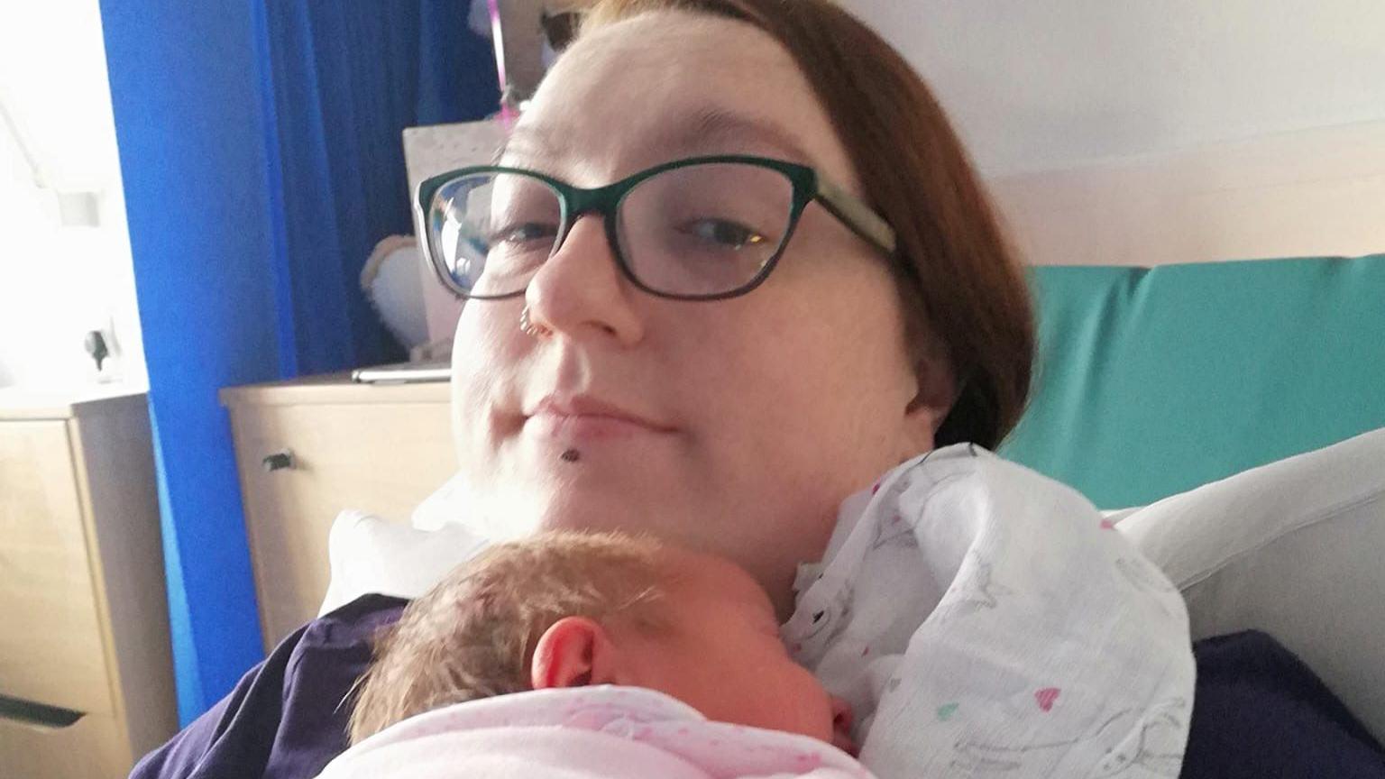 Debbie McCrudden holding her baby whilst lying on a hospital bed, which is green. 