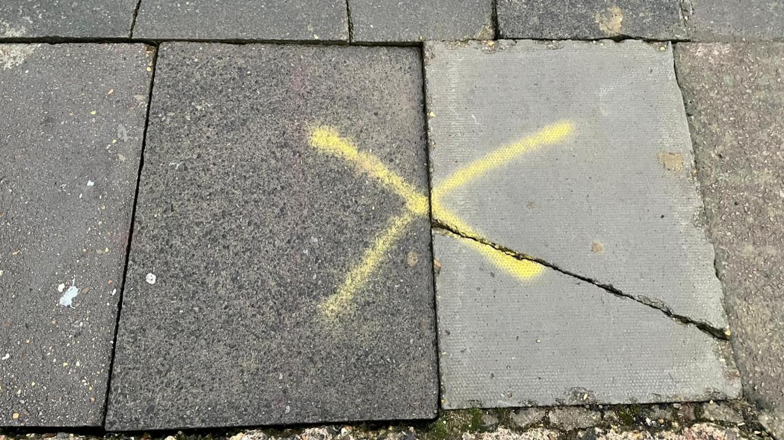 Cracked pavements with a spray-painted yellow cross marked across them 