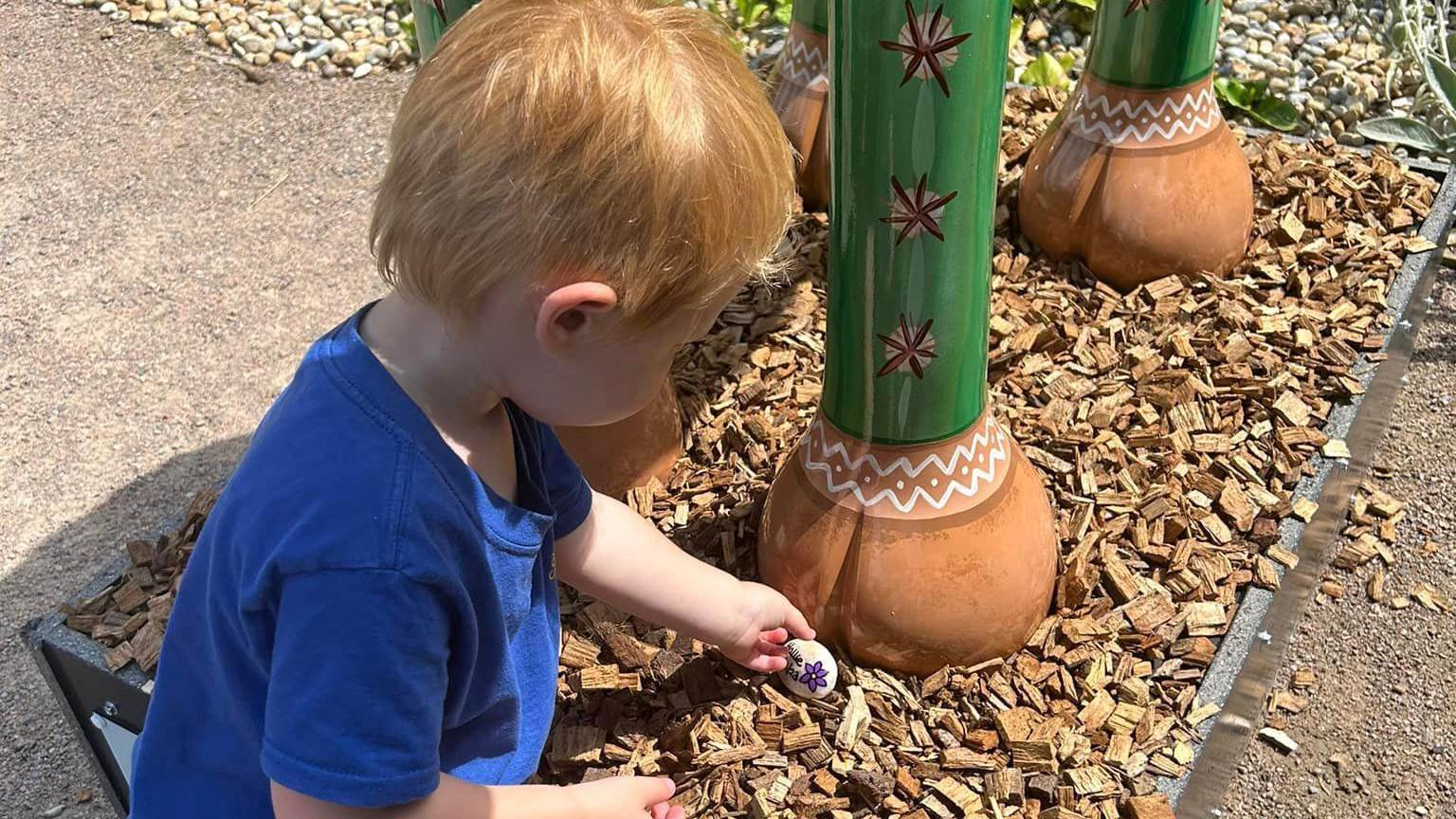 Toddler placing a decorated pebble on some bark chippings 