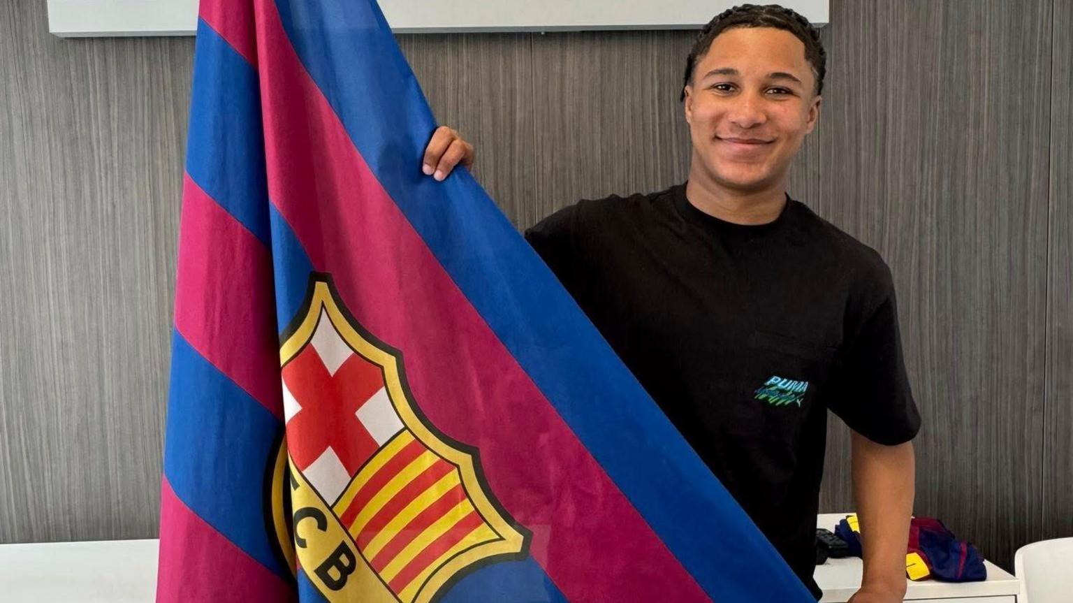 Ajay Tavares pictured with a Barcelona flag after signing for the club in February 2026