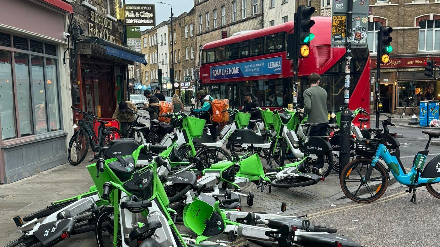 Around two dozen dockless e-bikes, some of which are overturned, block a pedestrian crossing and pavement in Shoreditch