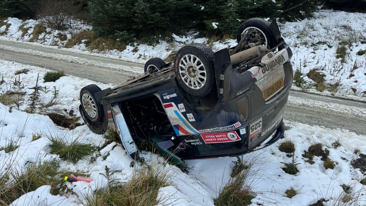 Hollie McRae's Mini lying upside down in a small ditch, surrounded by snow and ice.