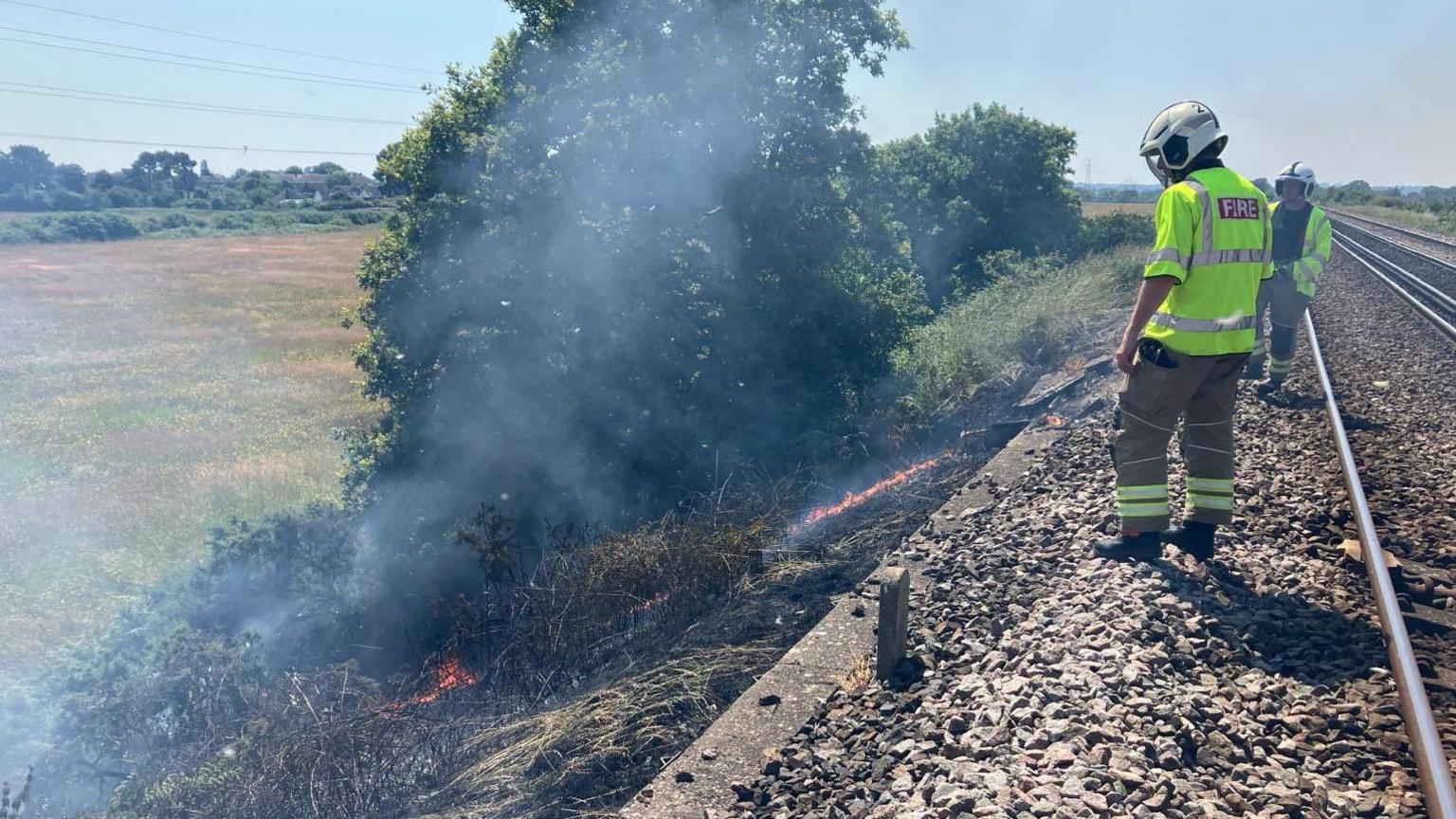 Fire fighters standing beside area of embankment on fire