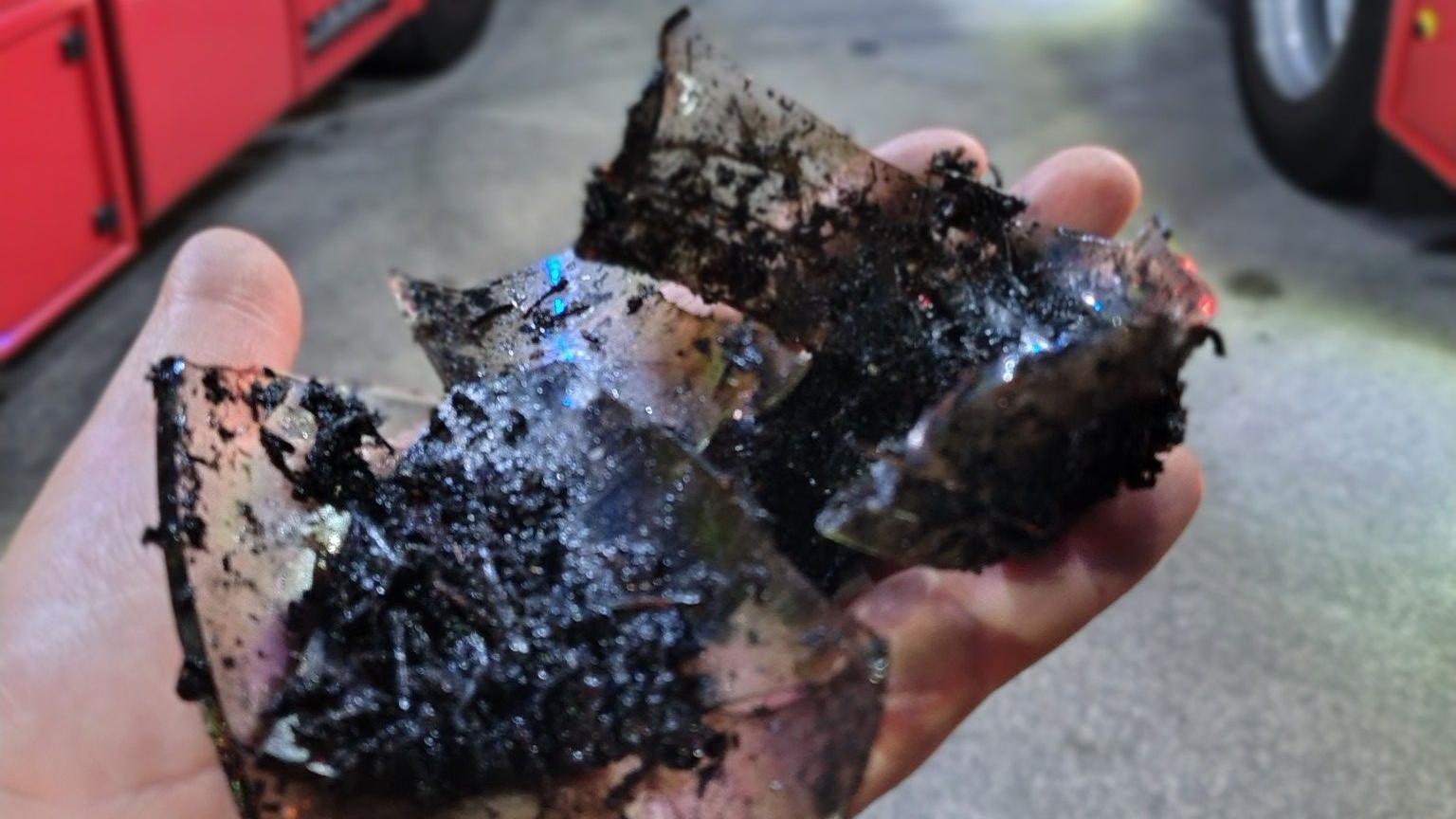 A hand holds shards of broken glass covered in mud.