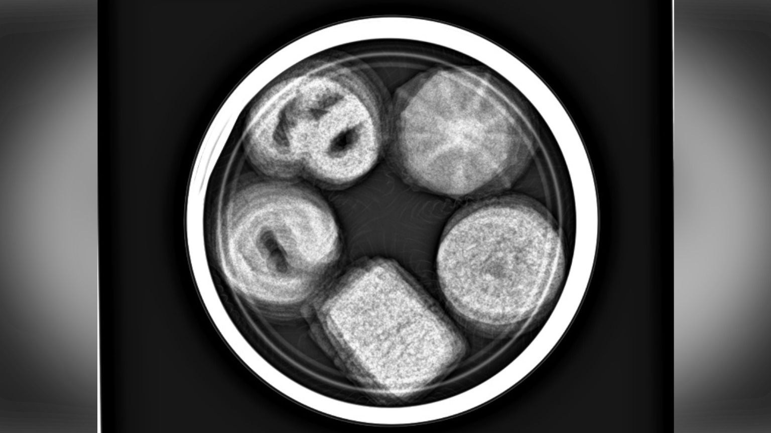 A round tin of biscuits with biscuits inside is pictured as a black and white X-ray.