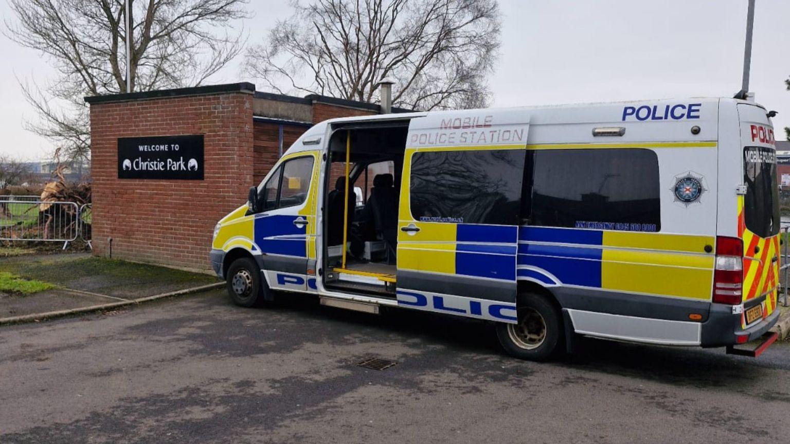 A mobile police station is parked with its side door open. The rear windows are tinted black and the van has police signage and coloured blue, yellow and white.