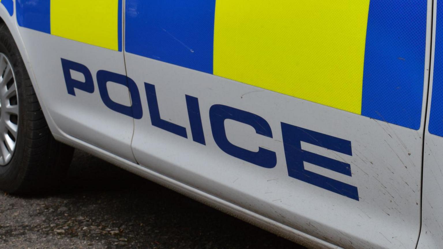 Police car, white with blue and yellow square along the side - seen from the front right tyre