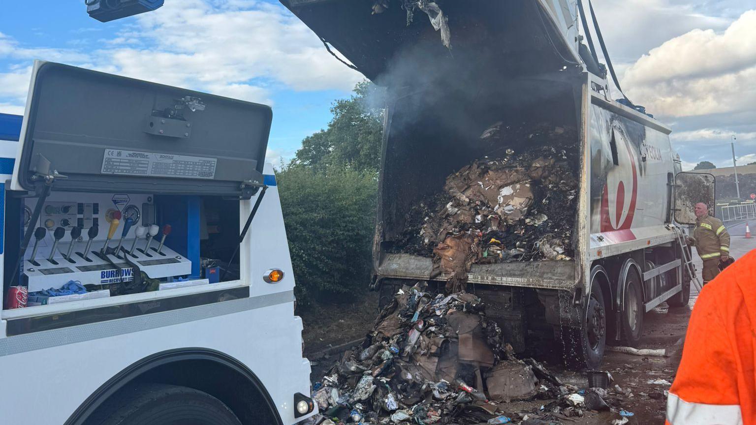 The rear of the bin lorry has been opened, with large amounts of burnt waste spilling out