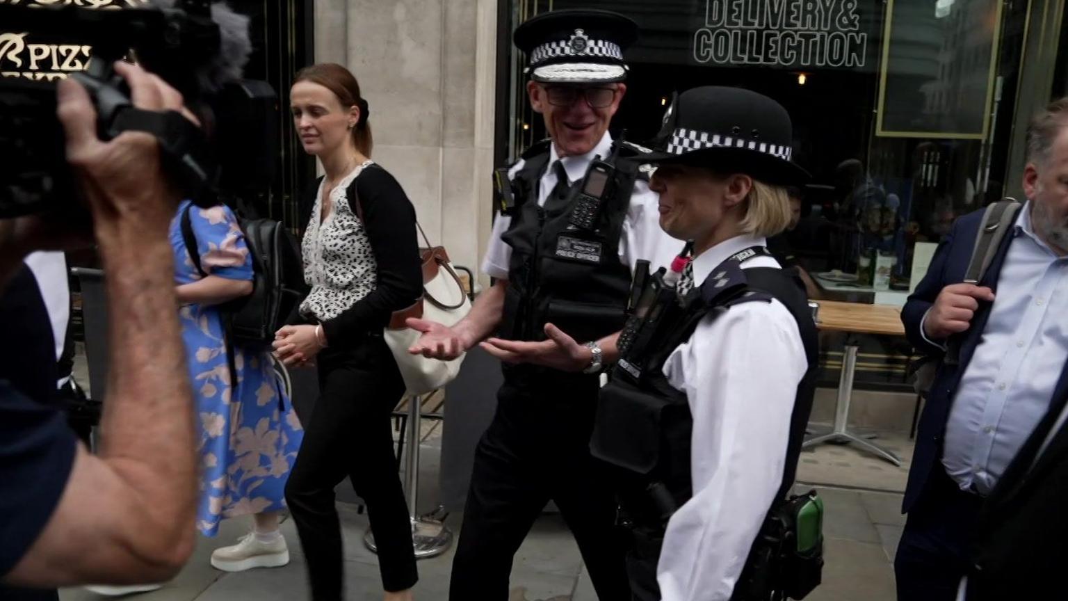 Sir Mark Rowley walks along the street with another officer whilst being filmed 