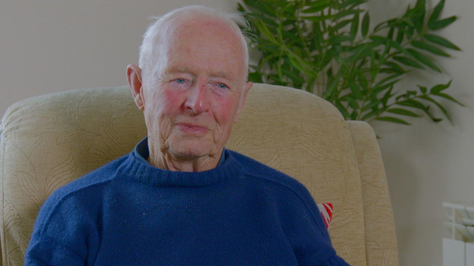 A man looking slightly off camera and wearing a blue jumper.