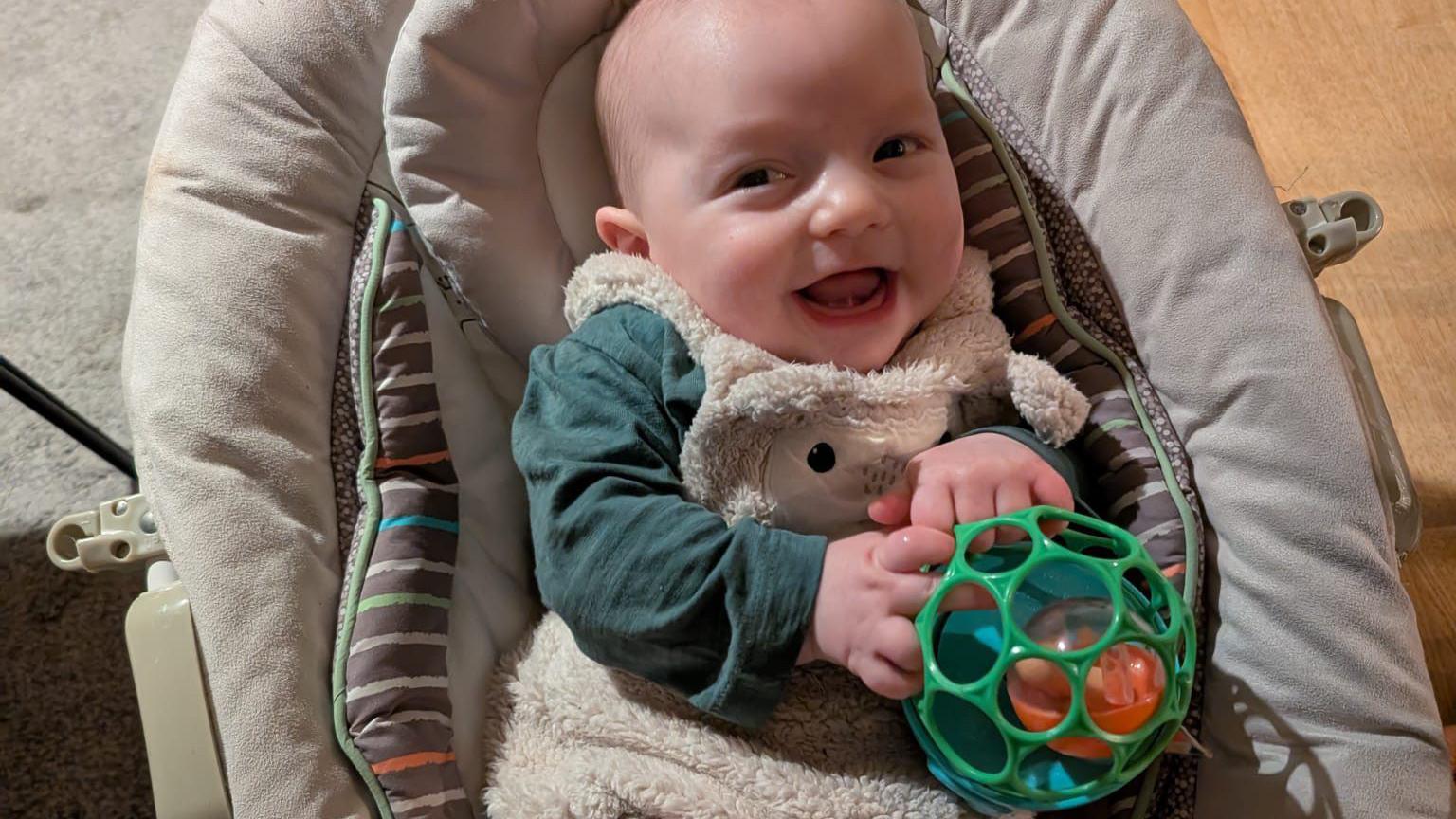 A photo of healthy baby Riley, holding a toy and smiling.