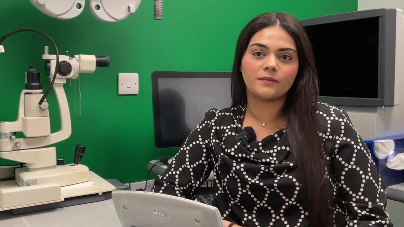 Woman with long black hair sat in Optician's office 