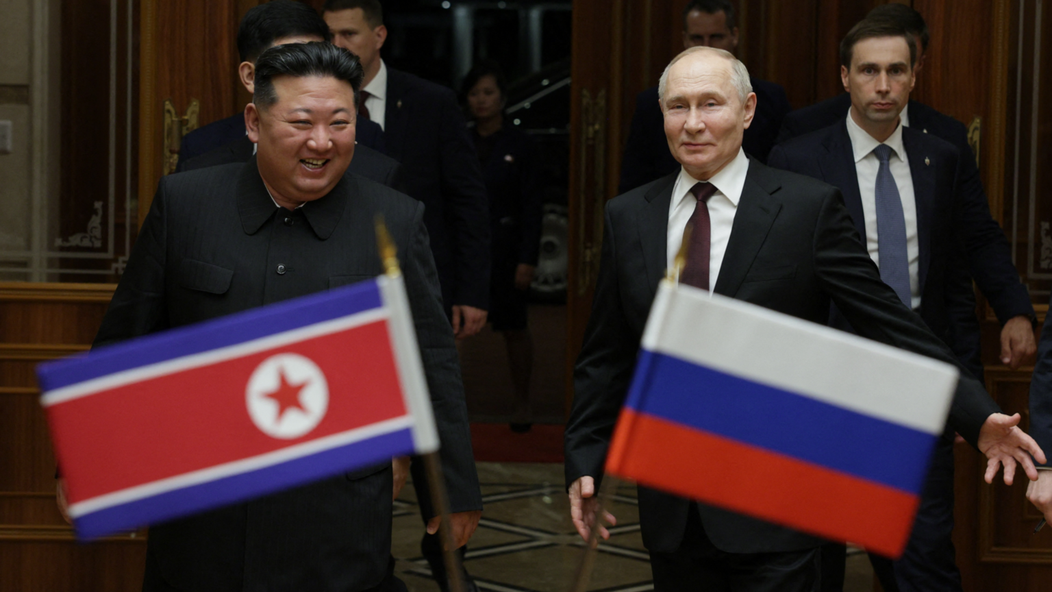 Kim Jong Un (left) smiles as he walks alongside Vladimir Putin (right) in front of the national flags of North Korea and Russia