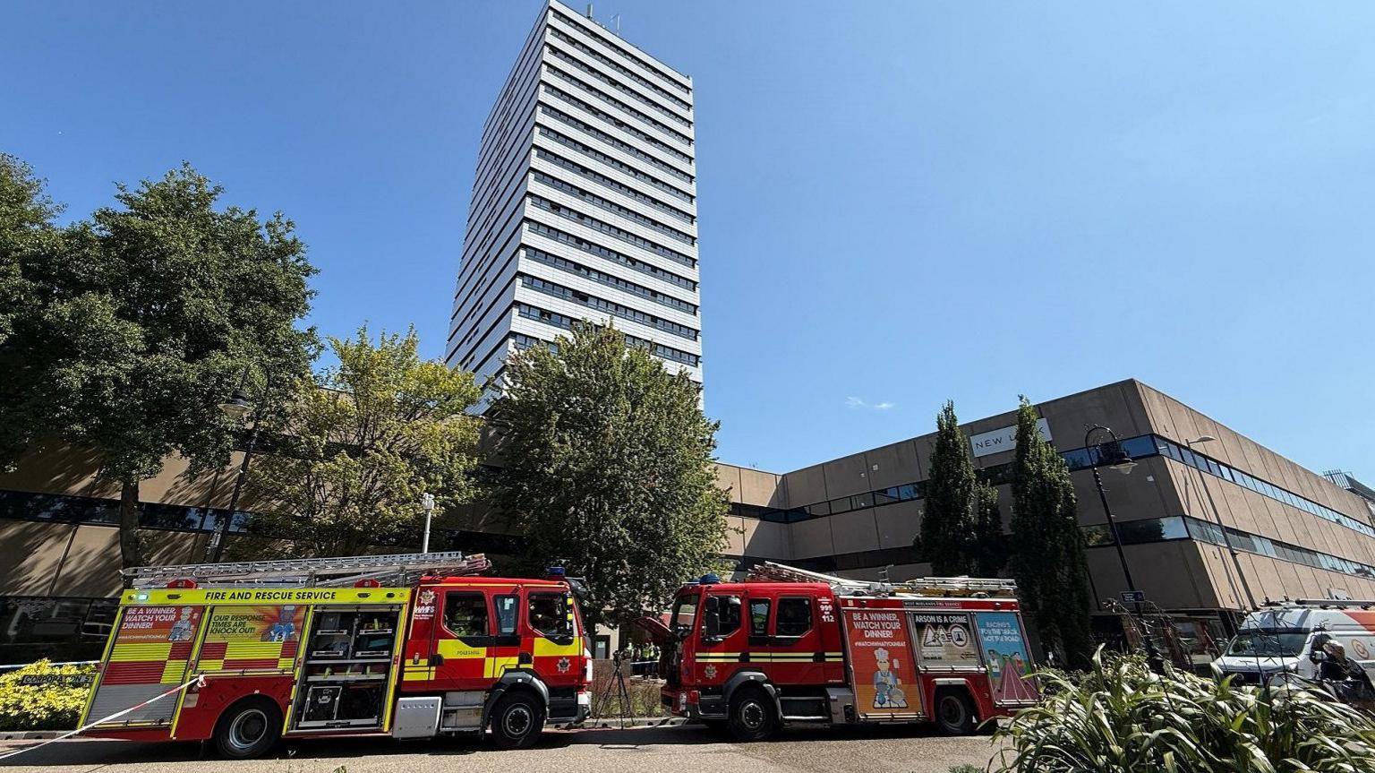 A number of fire trucks and cars parked outside the front of a tower block
