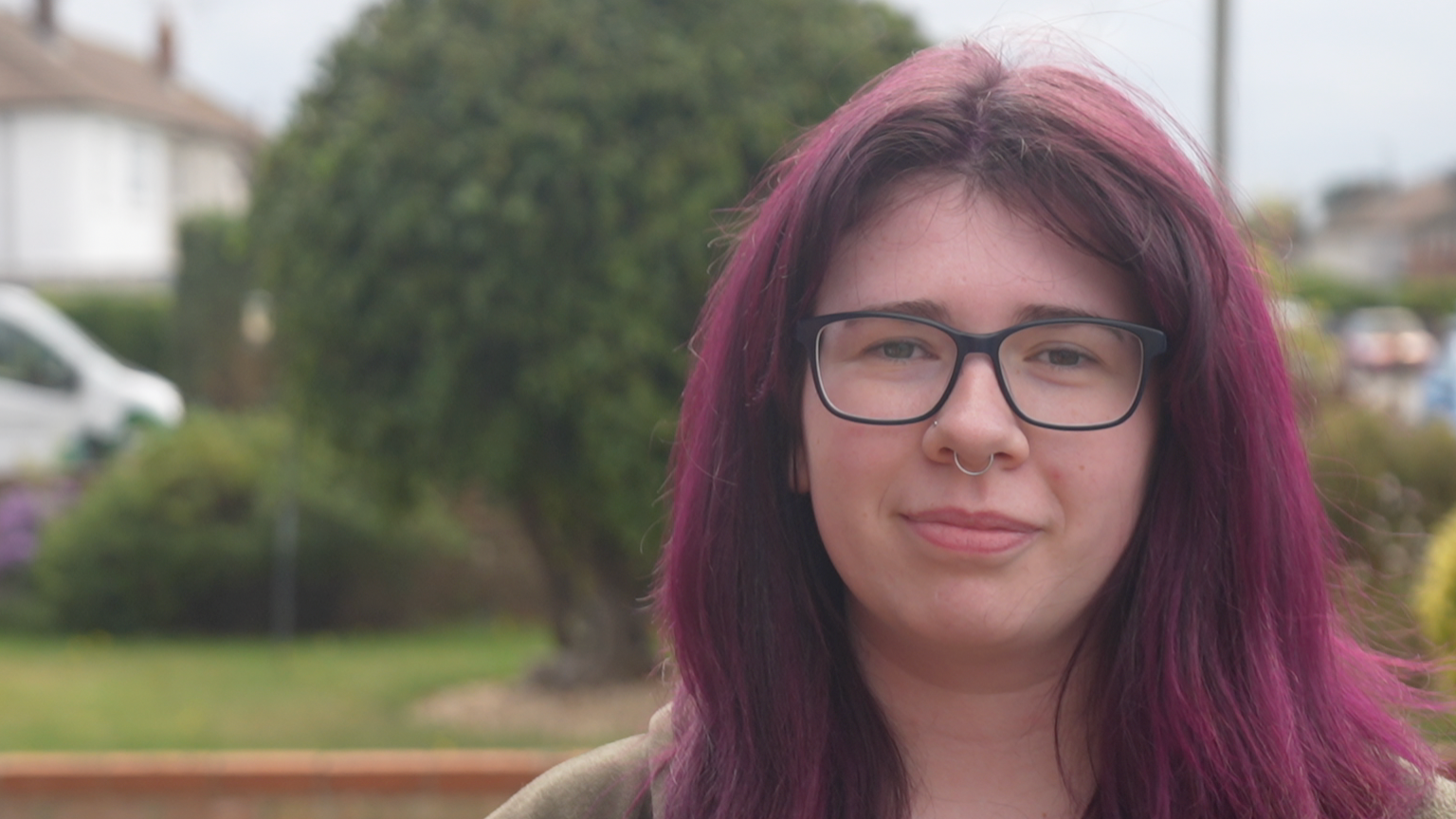 A head and shoulders image of Hannah Pain. She has purple hair and is looking into the camera.