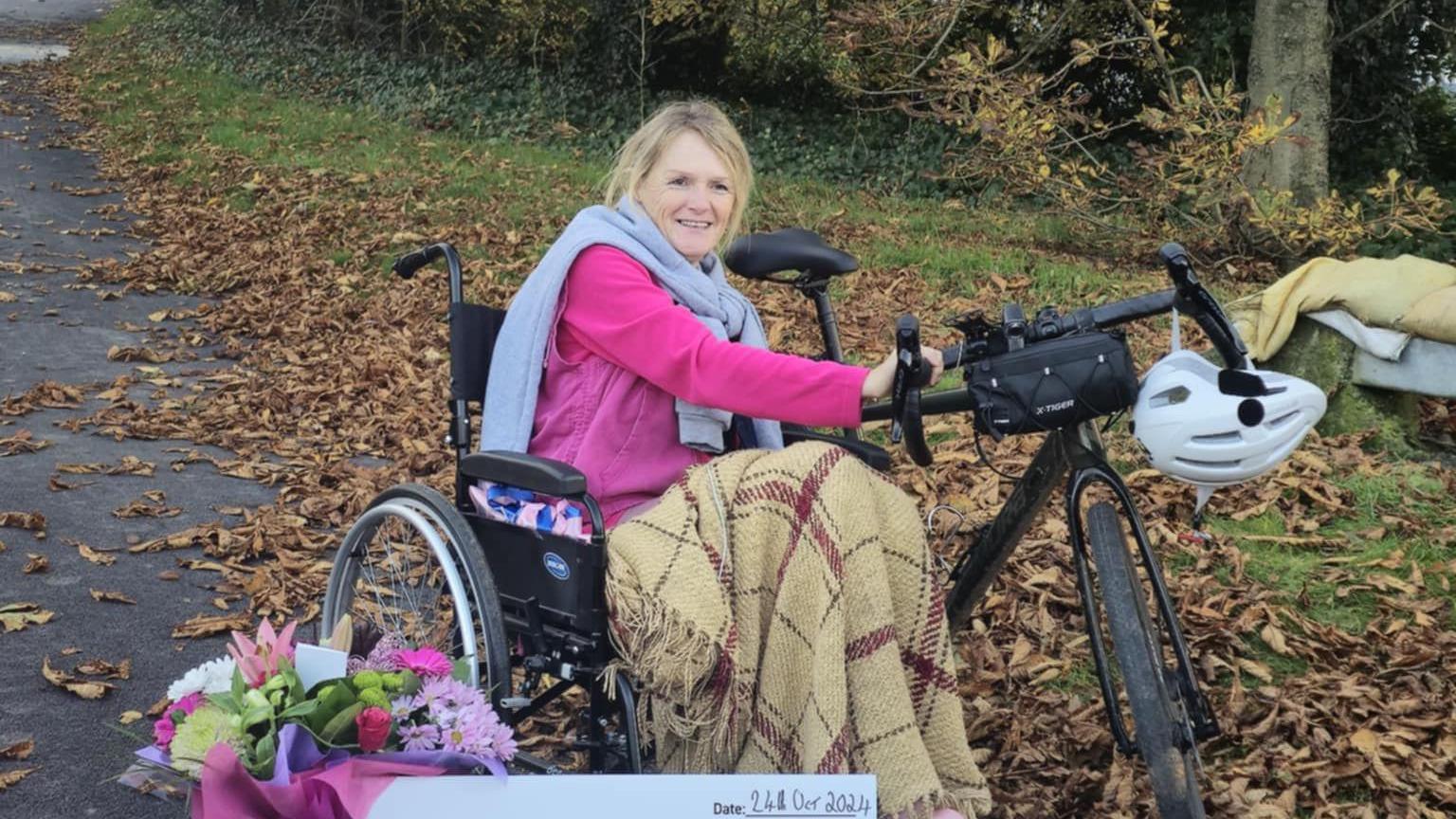 Alison Warner sits in a wheelchair and is smiling with her hands on a bike. 