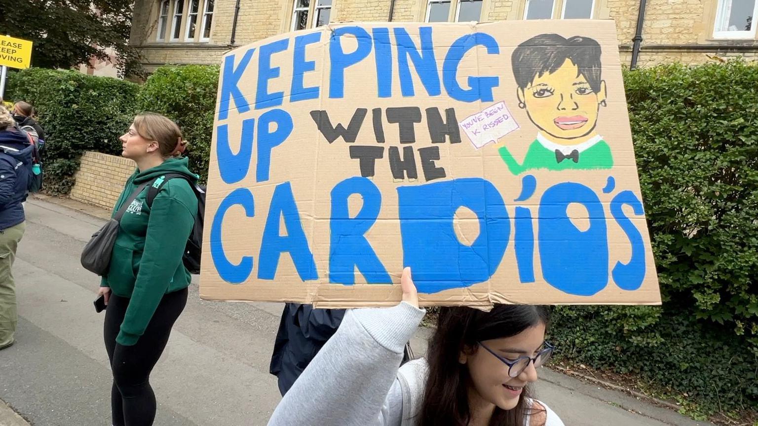 A girl holding up a sign saying 'Keeping up with the Cardios', along with a picture of Kris Jenner.