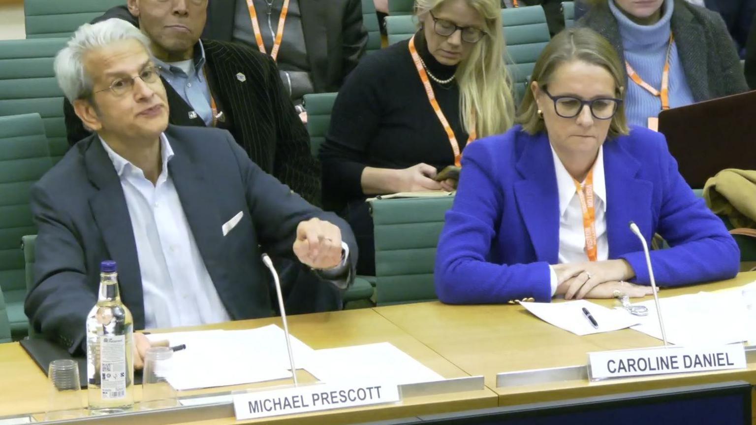 Former BBC editorial advisors Michael Prescott and Caroline Daniel in smart clothes being questioned by MPs