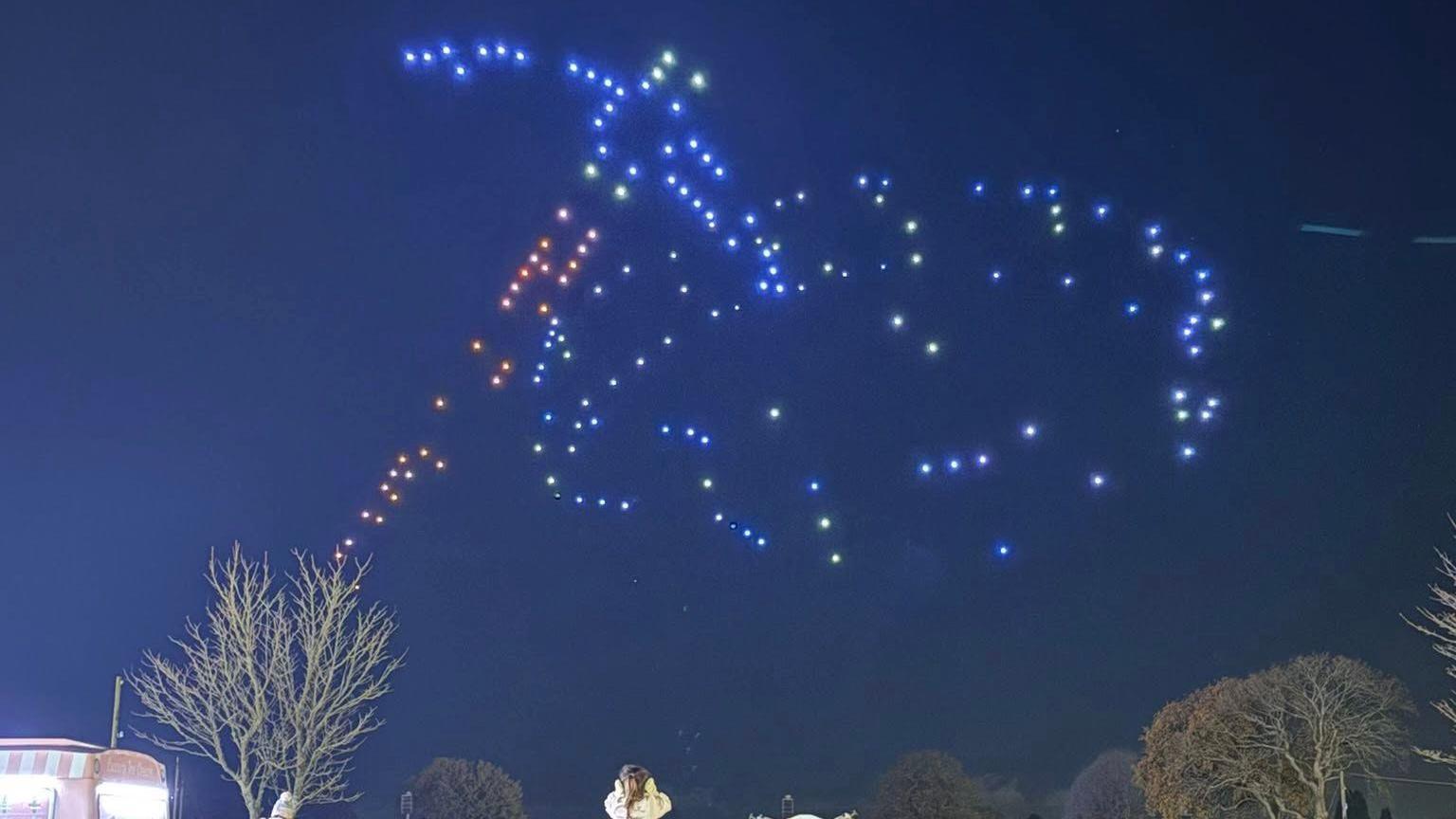 People standing in the Ardingly South of England showground look at an image of a hammer and a ring created in the sky by drones.