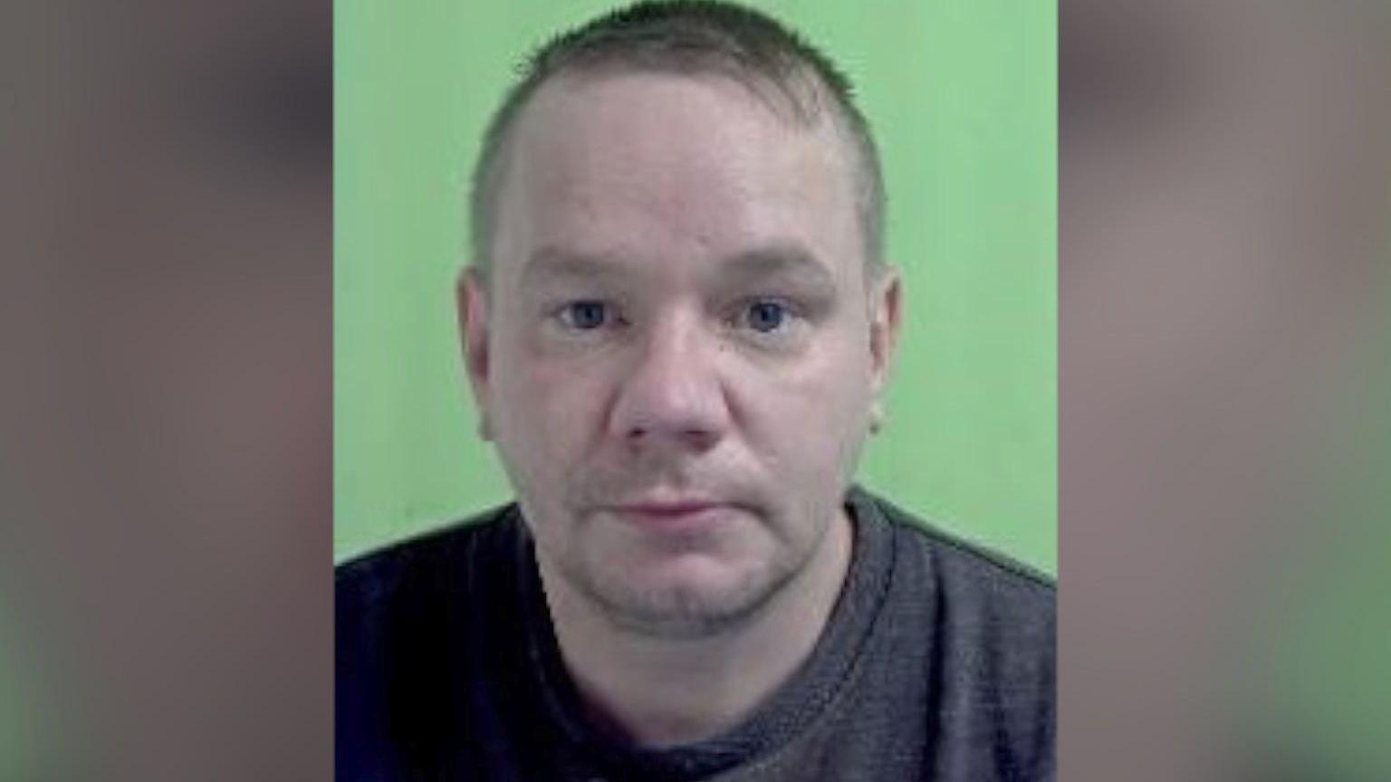 A middle aged man looks concerned at the camera in a police mugshot.