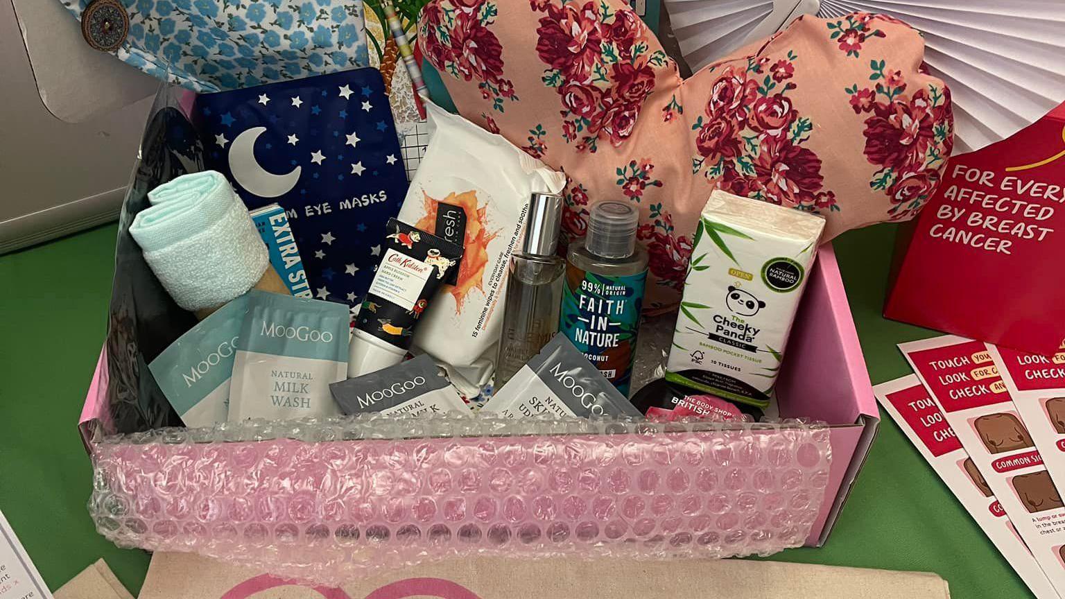 An open pink box containing items such as shampoo, tissues, eye masks and a flannel