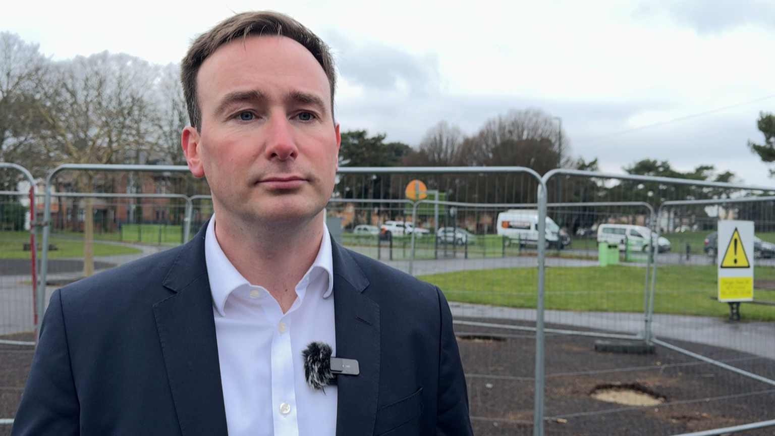 Tom is being interviewed in a children's park in Bournemouth. He is wearing a dark suit with a white shirt and no tie.