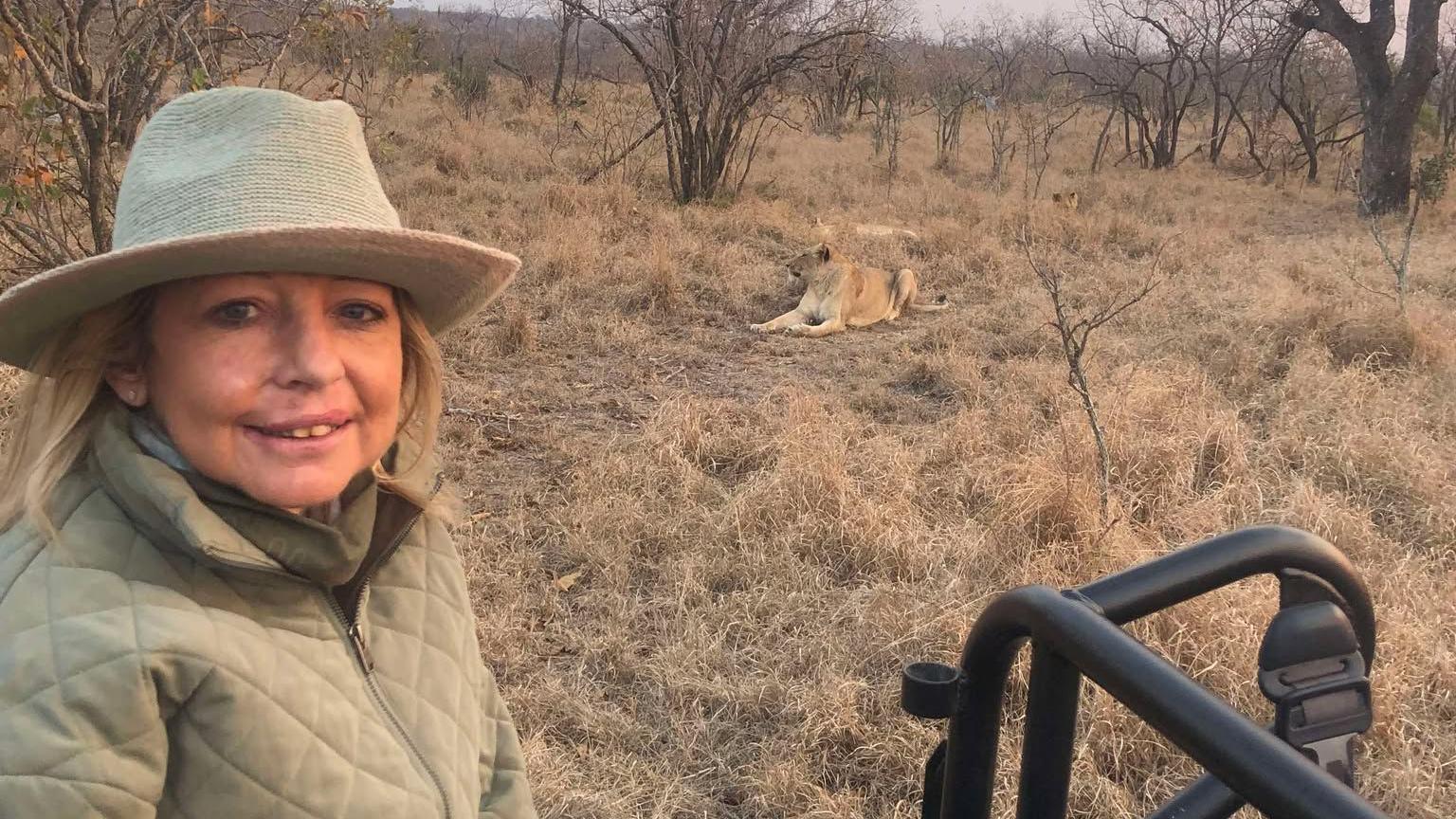 Allison pictured with a lioness on a safari, wearing a green jacket and hat she smiles towards the camera. 