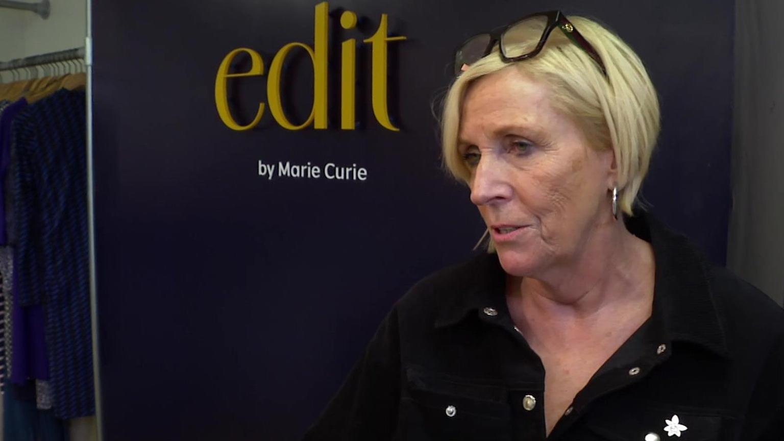 Jacqui Woolley, retail director at Marie Curie, speaking to a reporter at the charity shop. Behind Ms Woolley is the shop sign which reads 'edit by Marie Curie'.